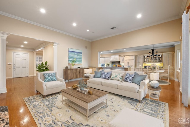 living room featuring ornamental molding, decorative columns, a chandelier, and light wood-type flooring