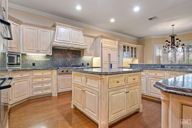 kitchen featuring built in appliances, a kitchen island, pendant lighting, and light brown cabinetry