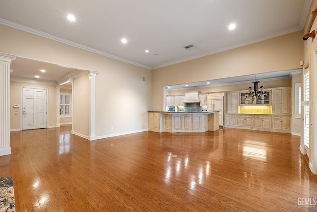 unfurnished living room with an inviting chandelier, ornamental molding, decorative columns, and light hardwood / wood-style flooring