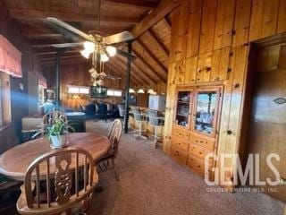 carpeted dining area with wood walls, ceiling fan, and lofted ceiling with beams