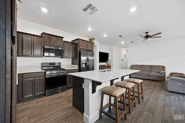 kitchen with sink, dark wood-type flooring, a center island with sink, stainless steel appliances, and a kitchen bar