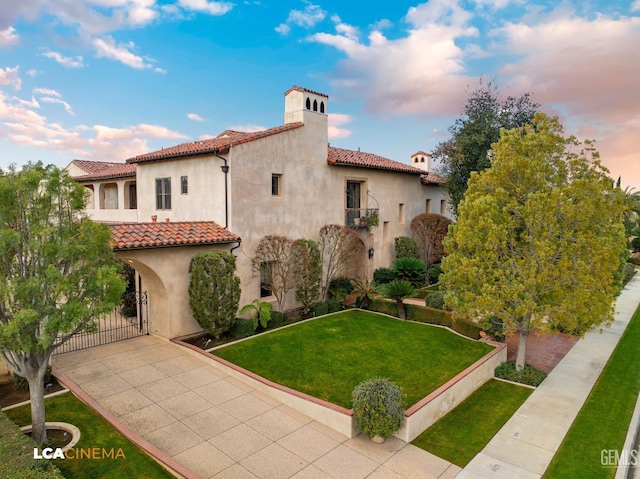 mediterranean / spanish-style home with a front yard, a gate, a chimney, and stucco siding