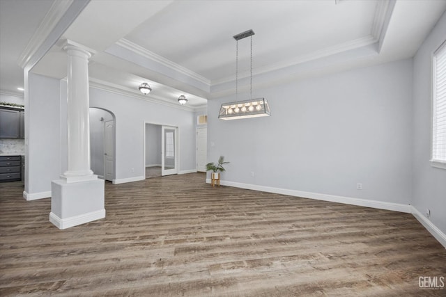 interior space with decorative columns, a tray ceiling, ornamental molding, and wood finished floors
