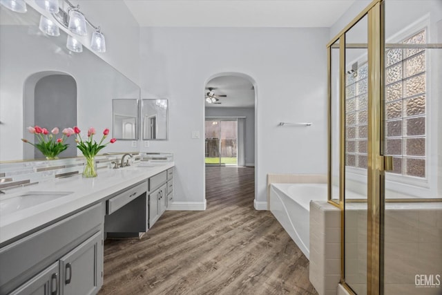 full bathroom featuring a bath, wood finished floors, double vanity, and a sink