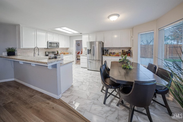 kitchen with backsplash, white cabinets, appliances with stainless steel finishes, light stone counters, and kitchen peninsula