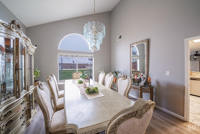 dining area with hardwood / wood-style flooring, a towering ceiling, and an inviting chandelier