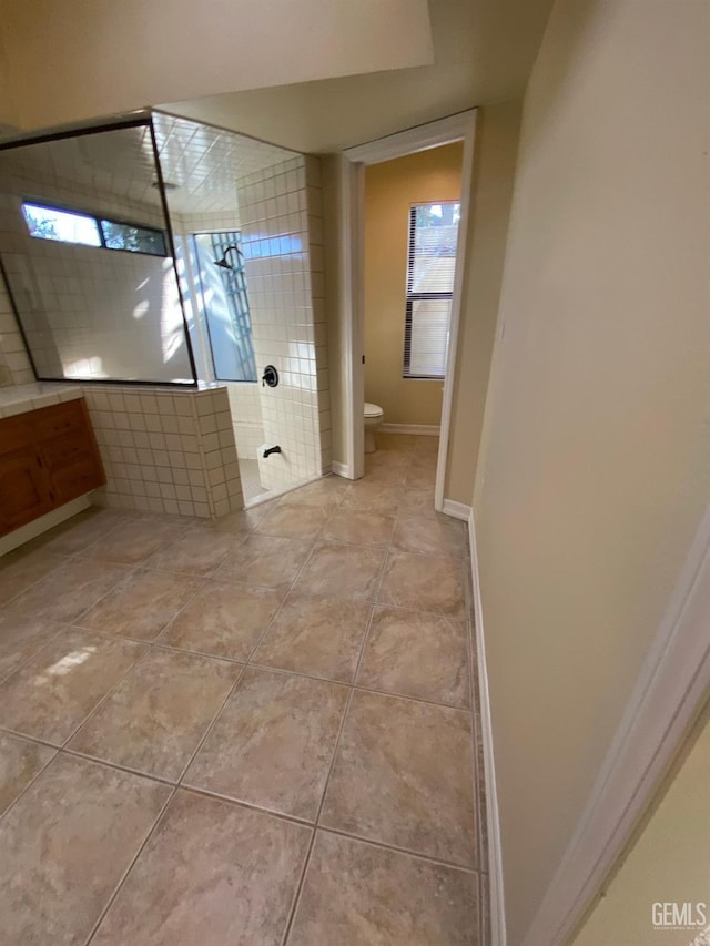 full bath with tiled shower, tile patterned floors, toilet, and baseboards