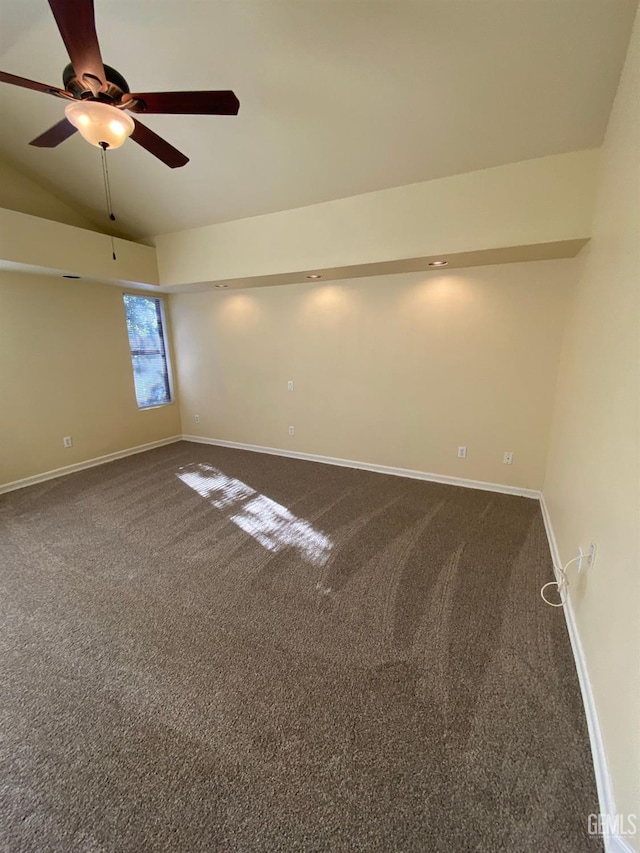 empty room featuring a ceiling fan, dark colored carpet, vaulted ceiling, and baseboards