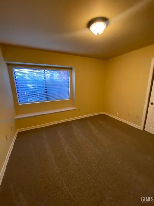 spare room featuring dark colored carpet and baseboards