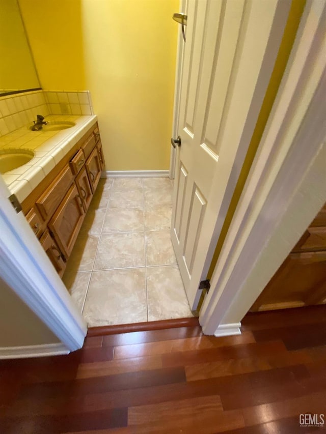 bathroom with double vanity, baseboards, a sink, and wood finished floors