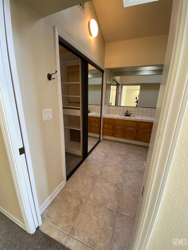 bathroom featuring a skylight, backsplash, vanity, baseboards, and tile patterned floors