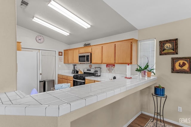 kitchen with kitchen peninsula, hardwood / wood-style floors, stainless steel appliances, and tile countertops