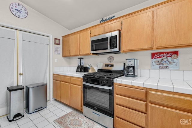 kitchen featuring tile counters, light tile patterned floors, lofted ceiling, and appliances with stainless steel finishes