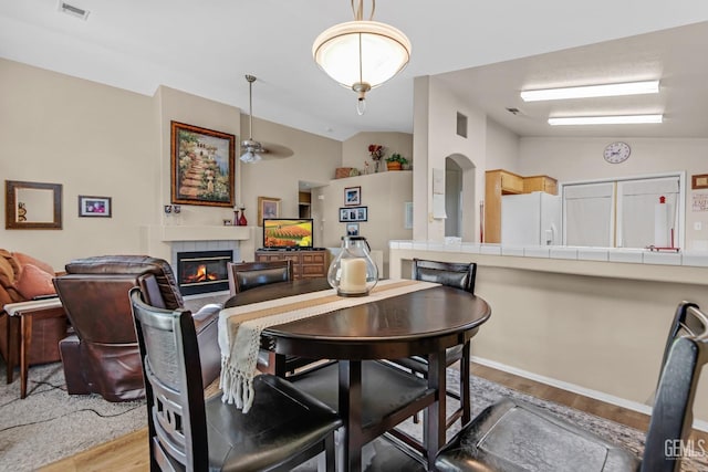 dining area with ceiling fan, light hardwood / wood-style floors, lofted ceiling, and a fireplace