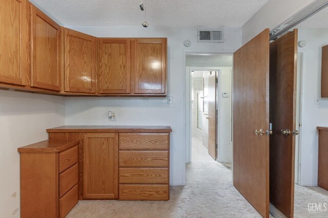 726 D St, Taft, CA 93268 - kitchen with brown cabinetry, visible vents, a textured ceiling, and light colored carpet