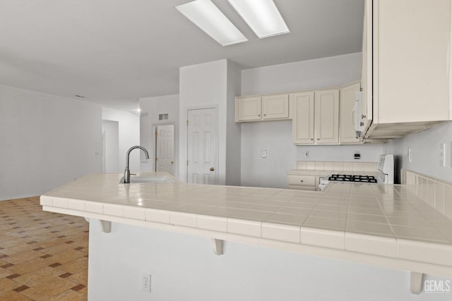 kitchen with a peninsula, white appliances, a sink, and tile countertops
