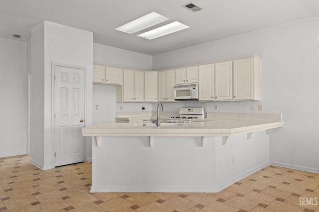 kitchen featuring tile countertops, stove, white microwave, and a sink