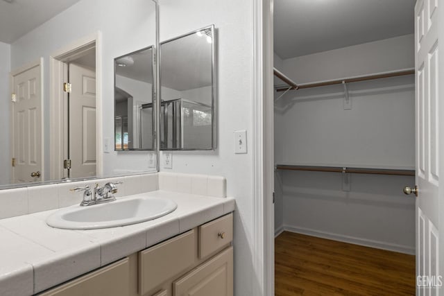 full bath with a spacious closet, an enclosed shower, vanity, and wood finished floors