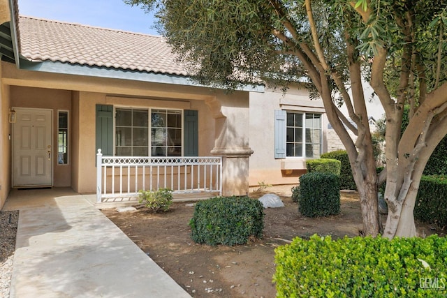 doorway to property featuring covered porch, a tiled roof, and stucco siding