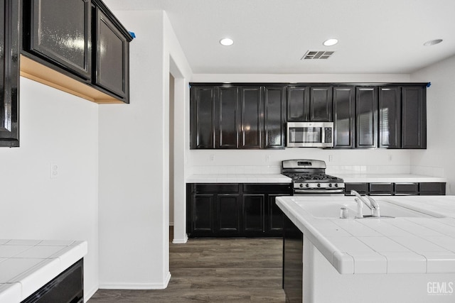 kitchen with appliances with stainless steel finishes, dark hardwood / wood-style flooring, tile counters, and sink