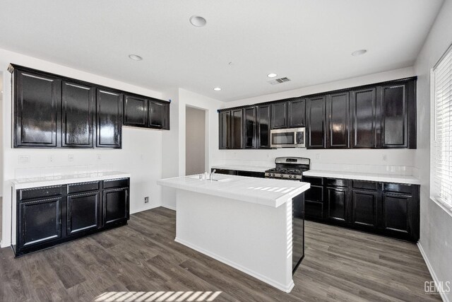 kitchen with wood-type flooring, stainless steel appliances, and a center island with sink