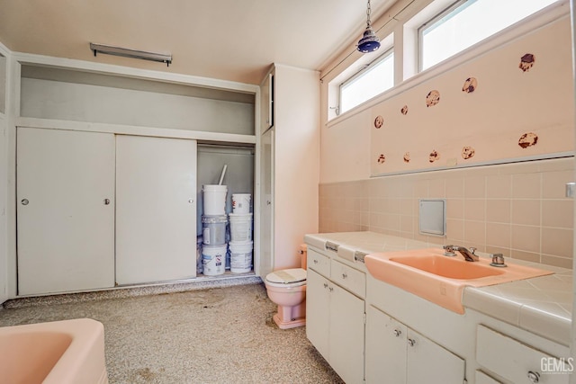 bathroom with vanity, backsplash, a bathing tub, toilet, and tile walls