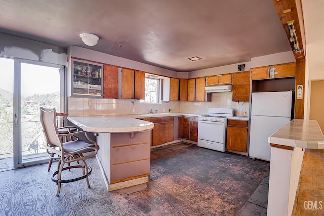 kitchen with tile countertops, a kitchen breakfast bar, white appliances, and kitchen peninsula