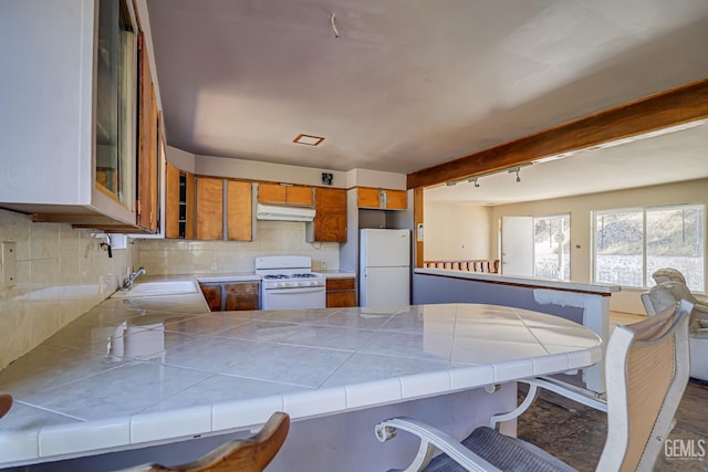 kitchen featuring tile counters, sink, backsplash, kitchen peninsula, and white appliances