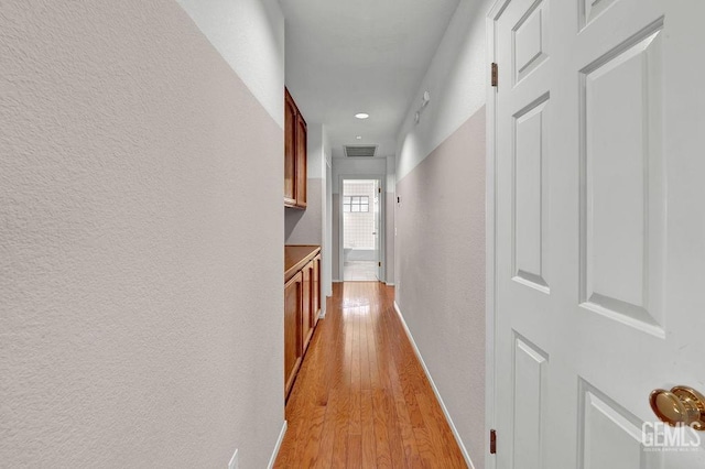 hall featuring light wood-style flooring, a textured wall, baseboards, and visible vents