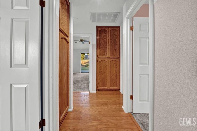 corridor featuring a textured wall, baseboards, visible vents, and light wood finished floors