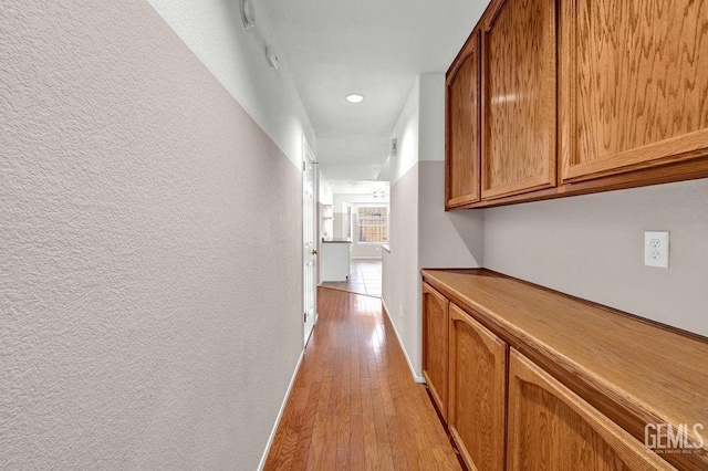 corridor featuring a textured wall, baseboards, and light wood-style floors