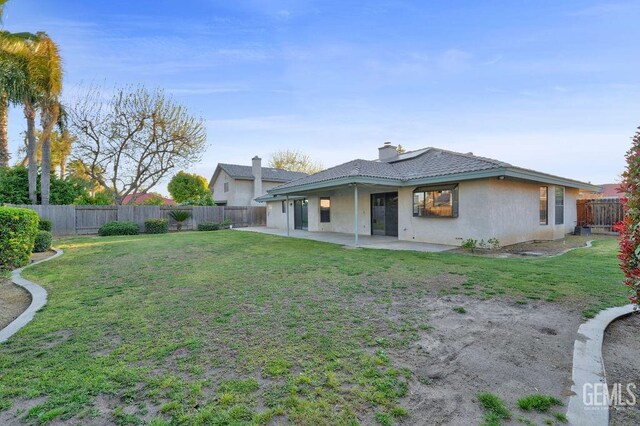 back of property featuring a patio, a chimney, a fenced backyard, stucco siding, and a lawn