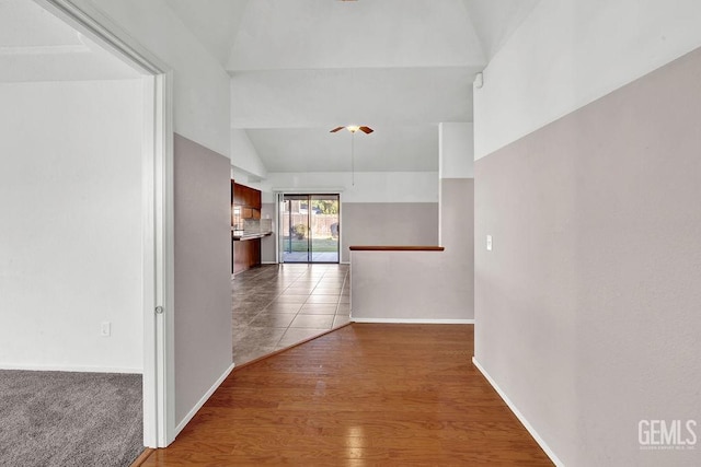 hallway with baseboards, vaulted ceiling, and wood finished floors