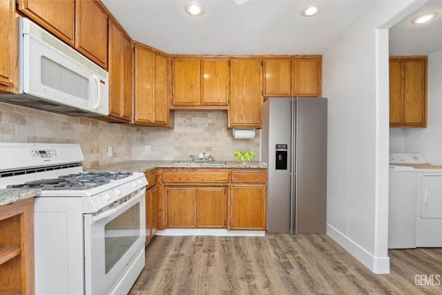 kitchen featuring washing machine and dryer, light wood-type flooring, decorative backsplash, white appliances, and a sink