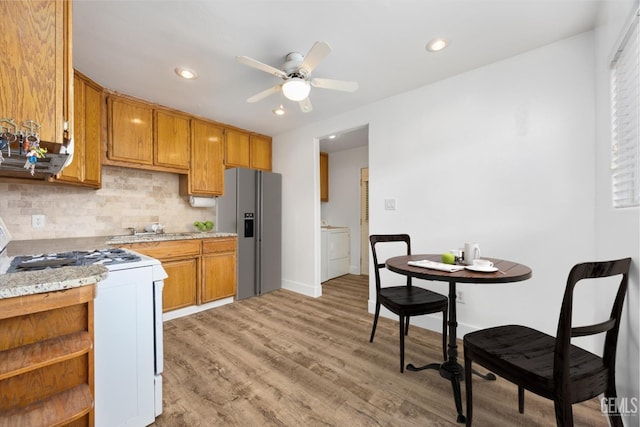 kitchen featuring stainless steel fridge with ice dispenser, white gas range oven, decorative backsplash, light wood-style flooring, and a ceiling fan