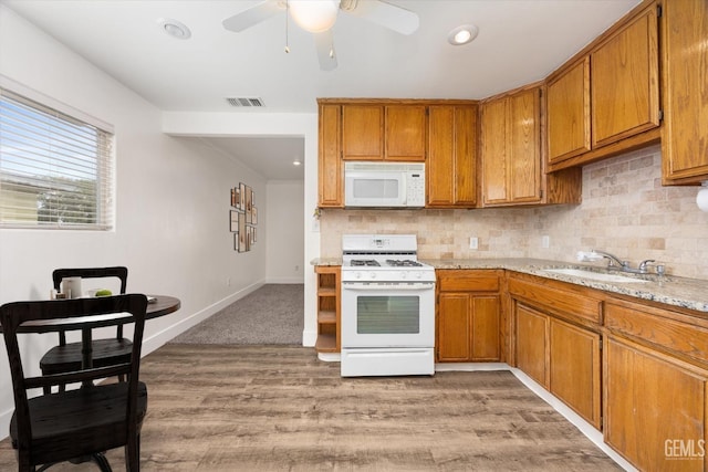 kitchen with white appliances, brown cabinetry, visible vents, a sink, and tasteful backsplash