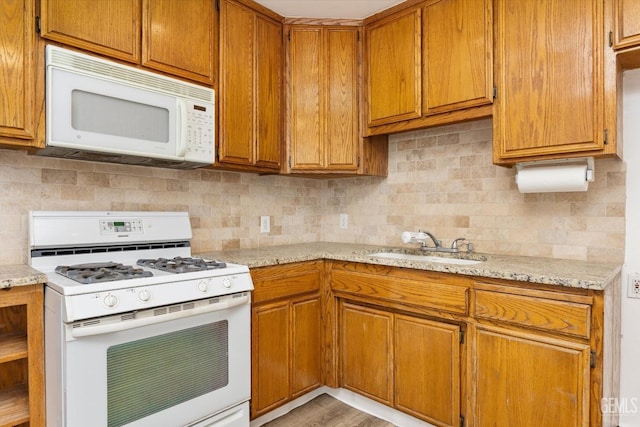 kitchen with backsplash, light stone counters, brown cabinetry, white appliances, and a sink