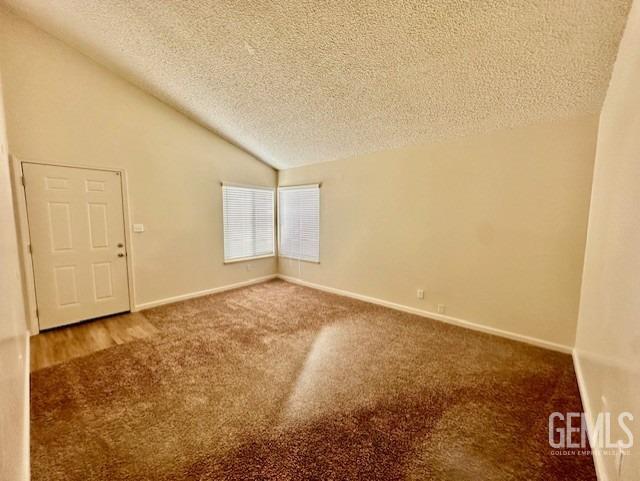 carpeted empty room featuring a textured ceiling and vaulted ceiling