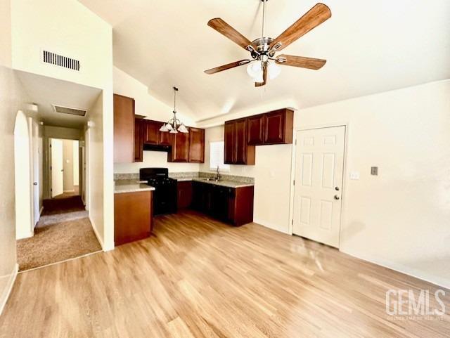 kitchen featuring hanging light fixtures, ceiling fan, light wood-type flooring, black gas range oven, and lofted ceiling