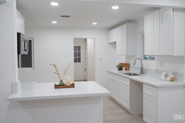 kitchen featuring light stone countertops, white cabinetry, sink, kitchen peninsula, and light hardwood / wood-style floors