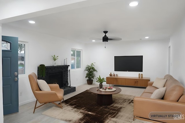 living room featuring ceiling fan, a healthy amount of sunlight, light wood-type flooring, and a brick fireplace