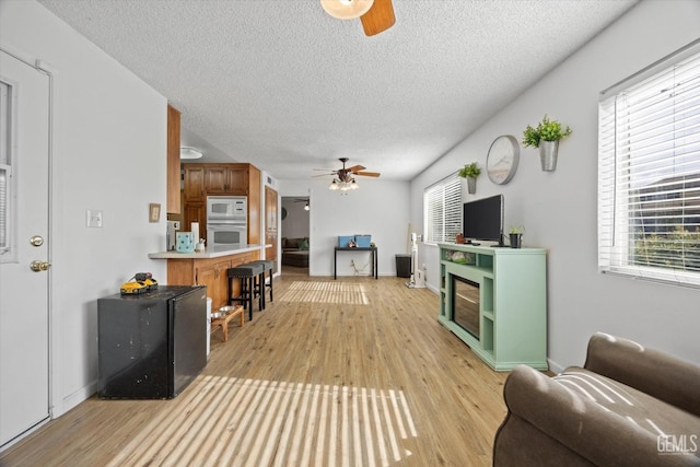 living room with ceiling fan, a textured ceiling, light wood-style flooring, and baseboards