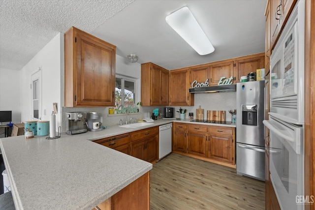 kitchen featuring brown cabinetry, a sink, a peninsula, and stainless steel fridge with ice dispenser