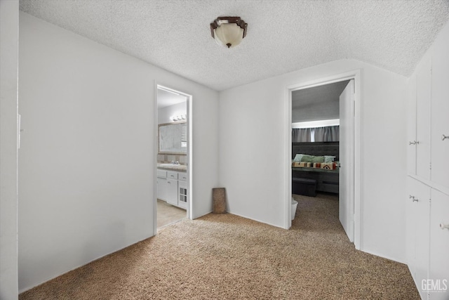 unfurnished bedroom featuring a sink, ensuite bath, a textured ceiling, and carpet flooring