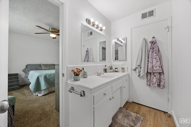 bathroom featuring visible vents, a ceiling fan, vanity, a textured ceiling, and wood finished floors