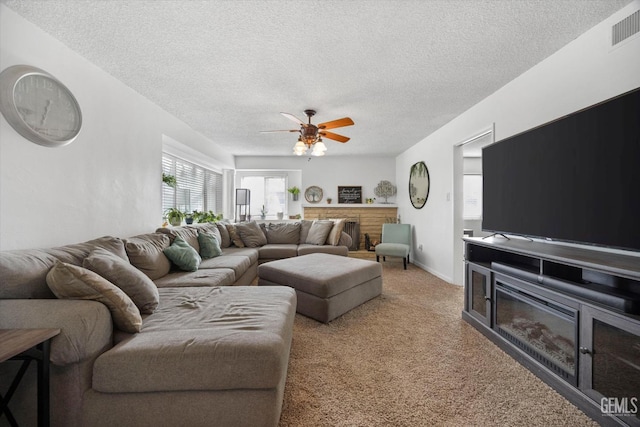 living area with a textured ceiling, light carpet, visible vents, a ceiling fan, and a brick fireplace