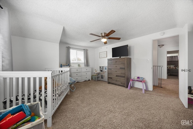 bedroom with a textured ceiling, ceiling fan, a crib, and carpet flooring