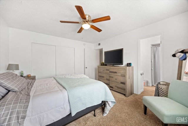 bedroom with light carpet, visible vents, a ceiling fan, a textured ceiling, and a closet