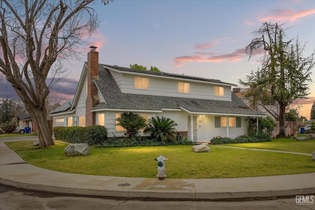 traditional-style house featuring driveway, a garage, solar panels, a chimney, and a yard