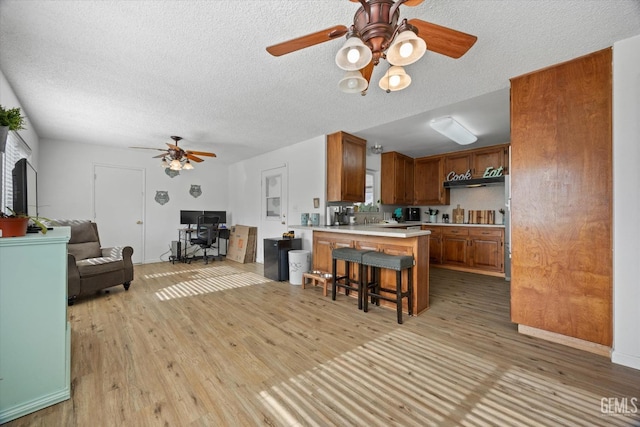 kitchen featuring brown cabinets, light countertops, open floor plan, a peninsula, and a kitchen breakfast bar